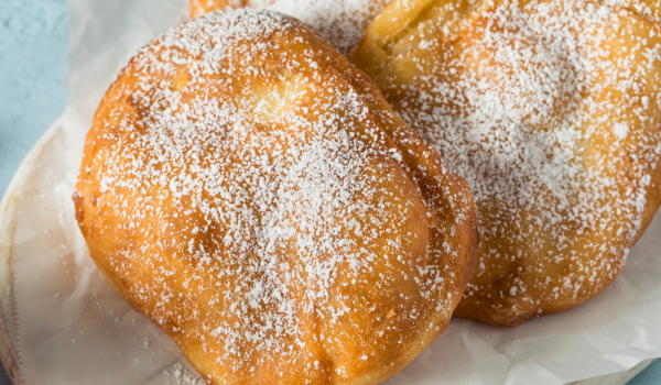 A plate of golden-brown fried treats lightly dusted with powdered sugar, ideal for a nostalgic and delicious dessert.