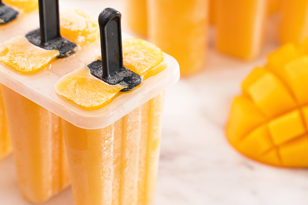 Frozen mango paletas still in their molds, showing a rich texture and fresh mango slices on top, capturing the essence of authentic Mexican-style frozen treats.