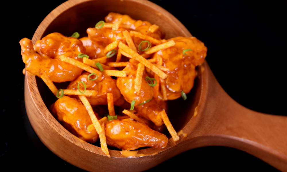 Spicy shrimp coated in a creamy red chili sauce, served in a wooden bowl and topped with crispy tortilla strips and fresh green onion for a flavorful twist.