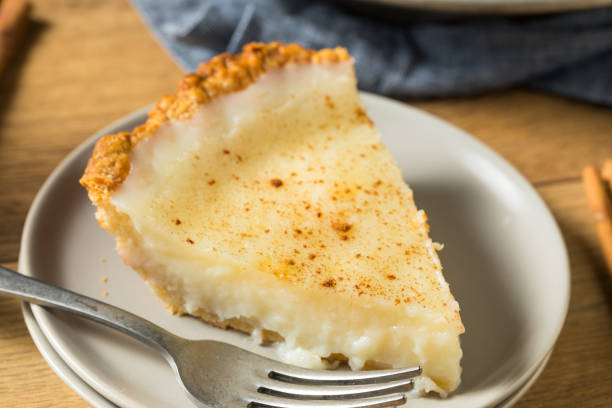 A close-up of a slice of Old Fashioned Custard Pie sprinkled with nutmeg on a neutral plate, showcasing its smooth and creamy texture with a flaky crust.