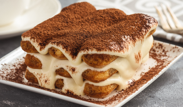 Rich and creamy tiramisu layers with mascarpone and cocoa on a square plate.