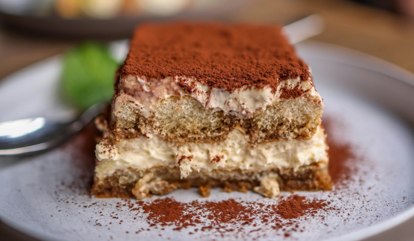 Delicious tiramisu dessert with creamy layers and a dusting of cocoa powder on a white plate