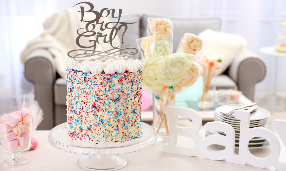 A colorful cake with vibrant sprinkles and a "Boy or Girl?" topper, placed on a glass cake stand in a beautifully decorated party setup.