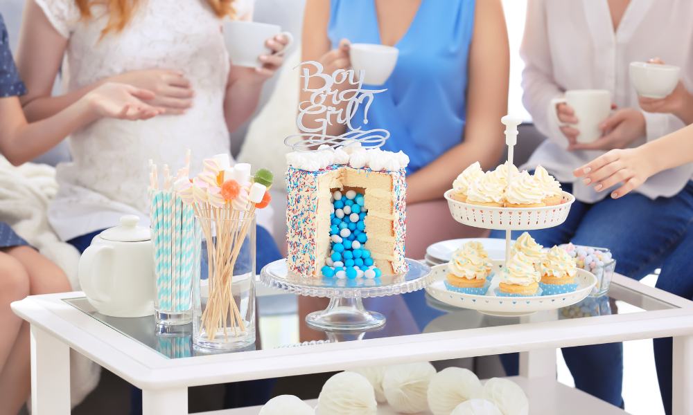 A dessert table featuring a centerpiece reveal cake surrounded by cupcakes, lollipops, and themed party decorations.