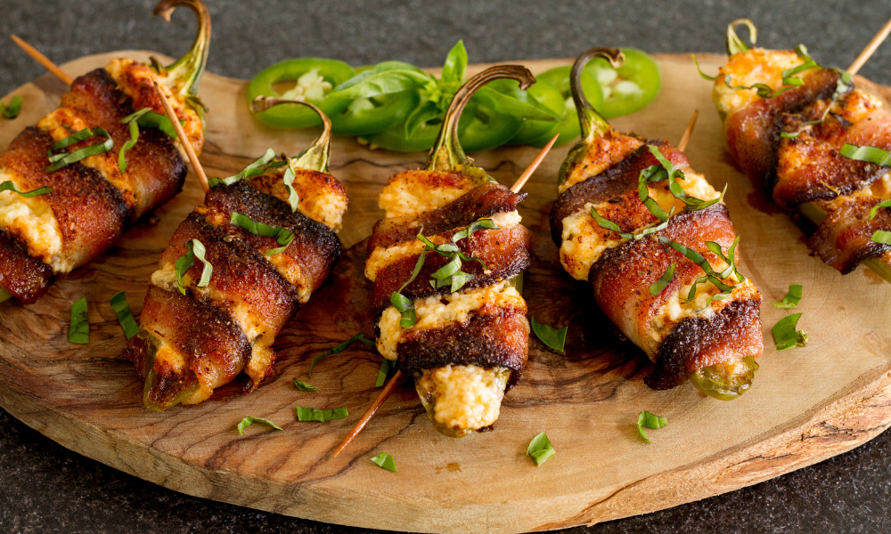 Bacon-wrapped jalapenos stuffed with cream cheese and spices, garnished with fresh basil.