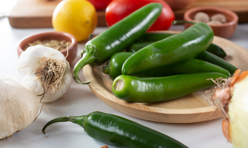 Serrano Pepper vs. Jalapeño: The Mexican Showdown of Two Peppers 12 Fresh serrano peppers on a wooden plate surrounded by ingredients like garlic, lemon, and tomatoes, ready for cooking