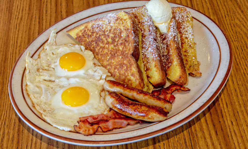 Classic breakfast plate with fried eggs, bacon, French toast, and breakfast sausage links