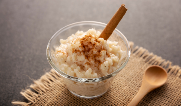 Delicious arroz con leche served in a glass bowl, sprinkled with cinnamon and garnished with a cinnamon stick on a rustic jute surface.