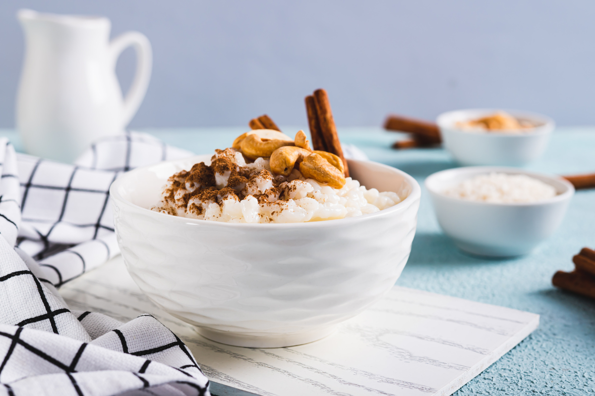 Close-up of a single white bowl filled with rich arroz con leche, sprinkled with cinnamon and cashews, set against a blue backdrop for a classic Mexican treat. spanish rice recipe