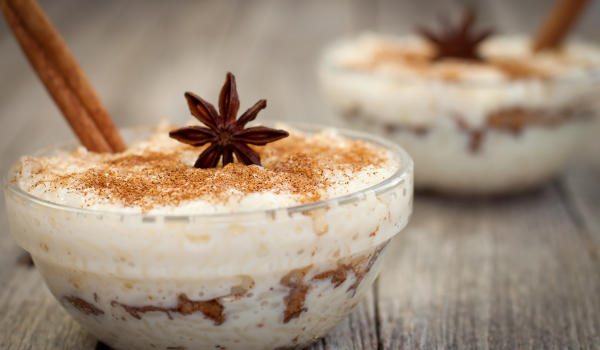 Mexican arroz con leche served in a glass bowl, decorated with a star anise and a cinnamon stick, showcasing layers of texture and color on a light wooden surface.