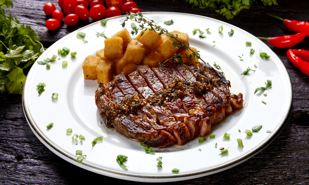 Grilled steak served with crispy potatoes and garnished with fresh herbs on a white plate.