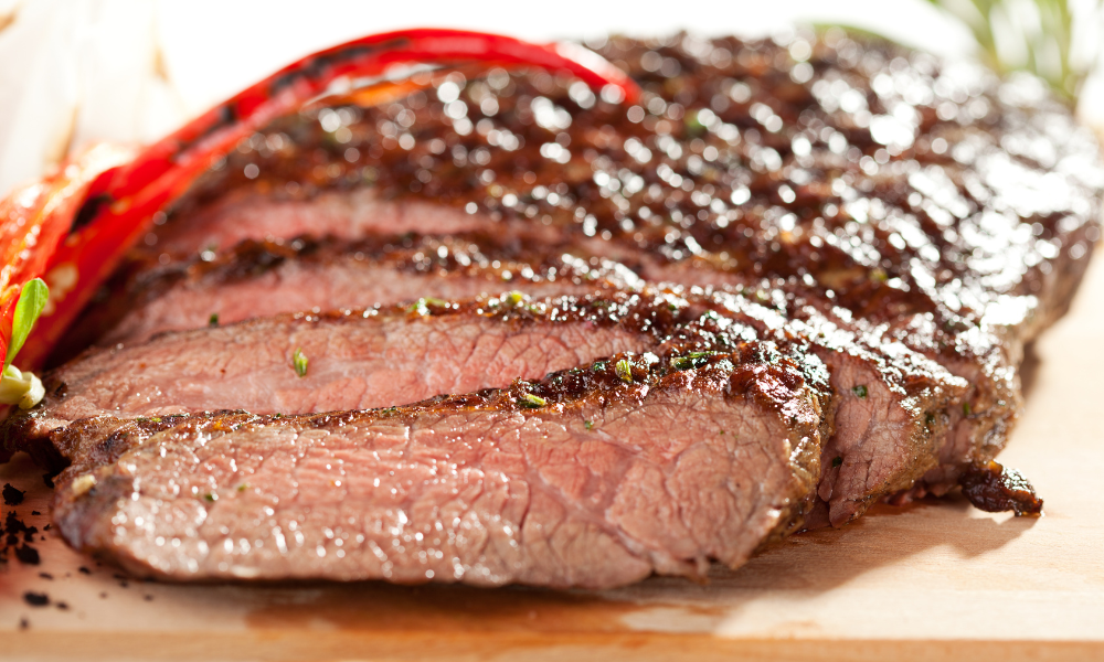 Juicy, sliced carne asada with a charred crust, garnished with red chili peppers on a wooden cutting board.