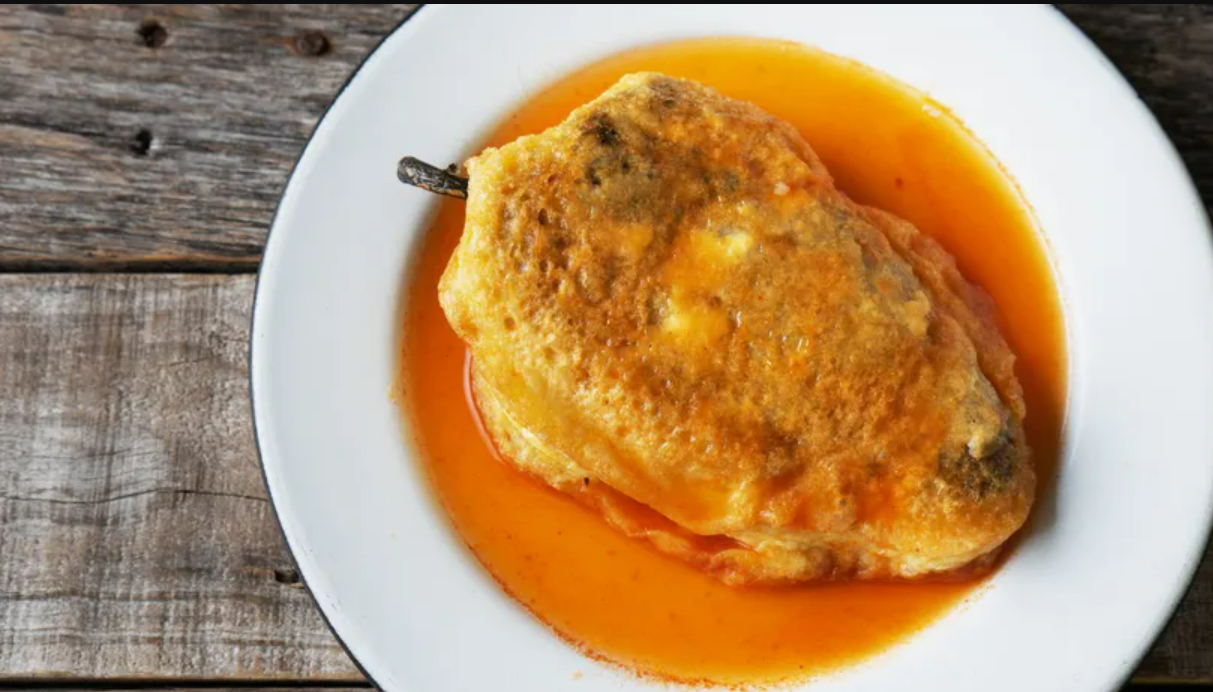 Golden-battered soaked in a vibrant red tomato sauce, served on a white plate with a rustic wooden table backdrop