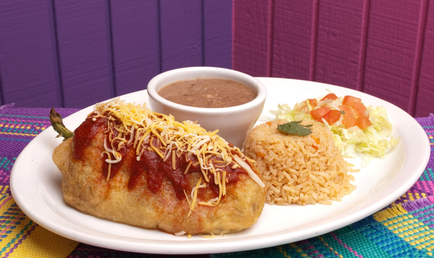 Golden chile relleno served with Mexican rice, refried beans, and fresh salad on a colorful tablecloth, topped with red sauce and shredded cheese for a vibrant and festive presentation.