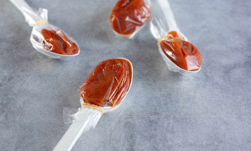 Discover Tamarind Candy at the Mexican Candy Store by Mexicrate 12 Close-up shot of plastic spoons each filled with soft, tangy tamarind candy wrapped in cellophane. These individually portioned spoons capture the sweet-and-sour flavor prized in many Mexican candies