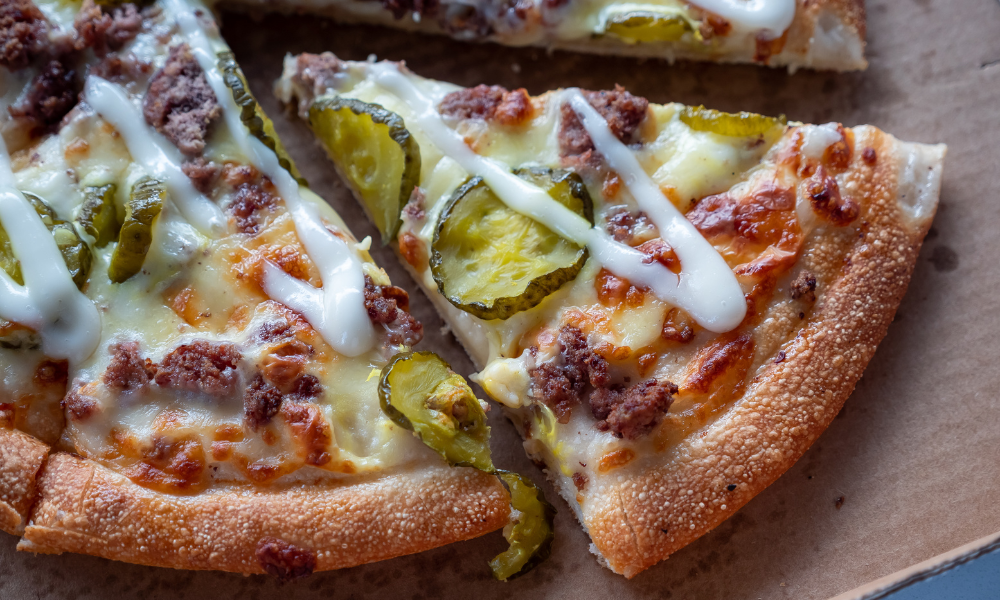 Close-up of a slice of pickle pizza topped with melted cheese, ground beef, and tangy dill pickle slices