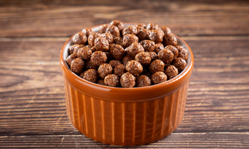 A rustic orange ramekin filled with crunchy chocolate protein cereal, displayed on a wooden table for a cozy vibe.