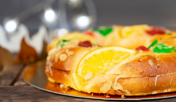 Rosca de Reyes with orange slices, candied fruits, and almonds, set on a golden plate with festive lights in the background