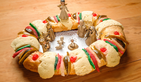 Traditional Rosca de Reyes decorated with candied fruits and figurines of the Three Wise Men placed in the center, presented on a wooden table.
