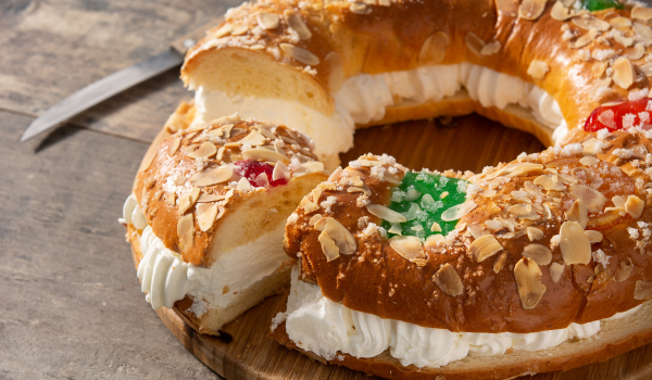Rosca de Reyes cut open to reveal a cream filling, topped with almonds and colorful candied fruits on a rustic wooden surface