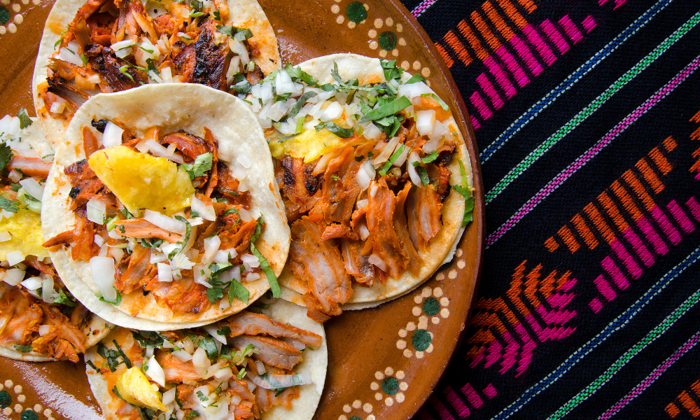 Delicious tacos al pastor with pineapple, onions, and cilantro on a colorful Mexican tablecloth.