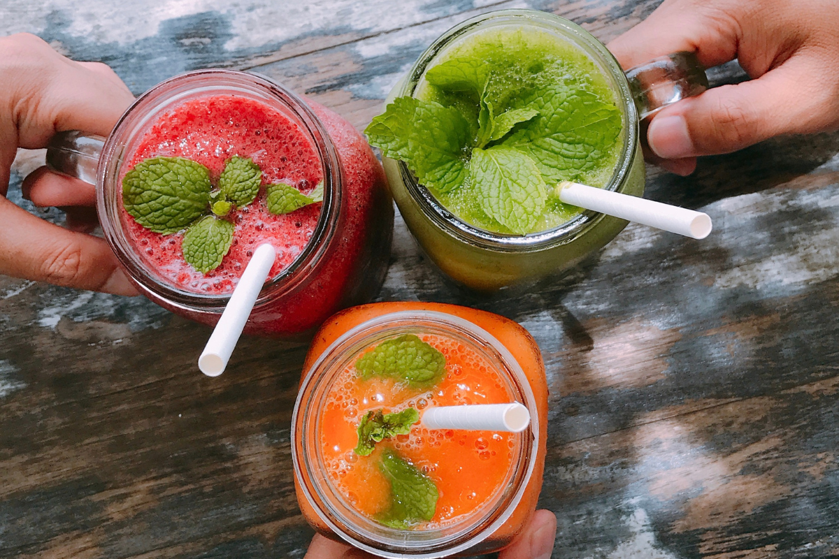 Three colorful smoothies (red, green, and orange) in glass jars topped with mint leaves, perfect for a refreshing and healthy tropical smoothie.